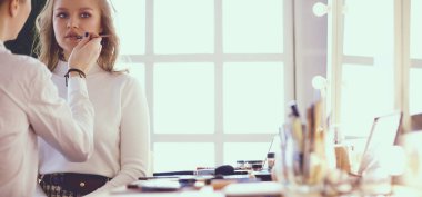 Makyaj sanatçısı genç ve güzel gelinin makyajını yapıyor.