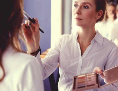 Makyöz, genç bir kadının profesyonel makyajını yapıyor.