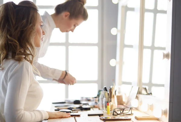 Make-up artist applying white eyeshadow in the corner of models eye and holding a shell with eyeshadow on background — 스톡 사진