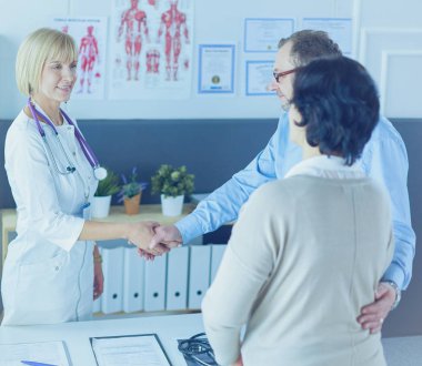 Kadın doktor bir hastanın elini sıkıyor ve gülümsüyor.