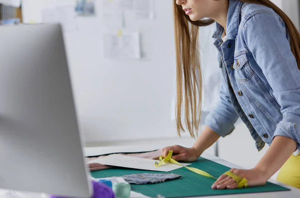 Krásná módní návrhářka stojící u stolu ve studiu — Stock fotografie