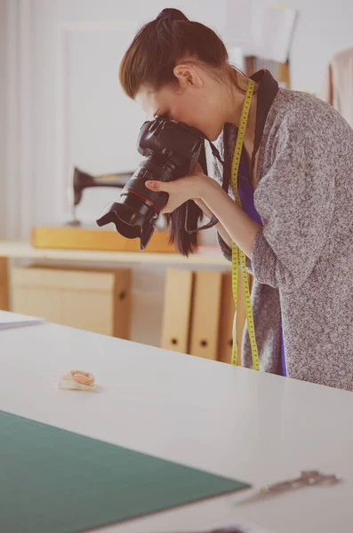 Mujer joven diseñadora de pie cerca del lugar de trabajo y fotografiándolo en una cámara digital — Foto de Stock