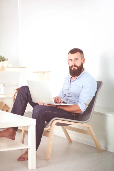 Jonge man zittend in de stoel en werken op laptopcomputer geïsoleerd op witte achtergrond — Stockfoto