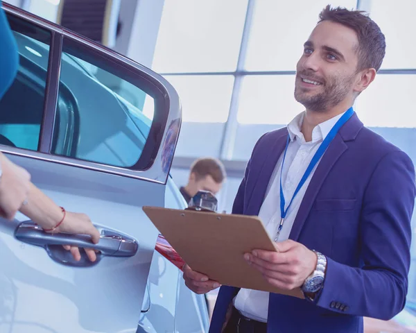 Distribuidor de mujer se para cerca de un coche nuevo en la sala de exposición — Foto de Stock