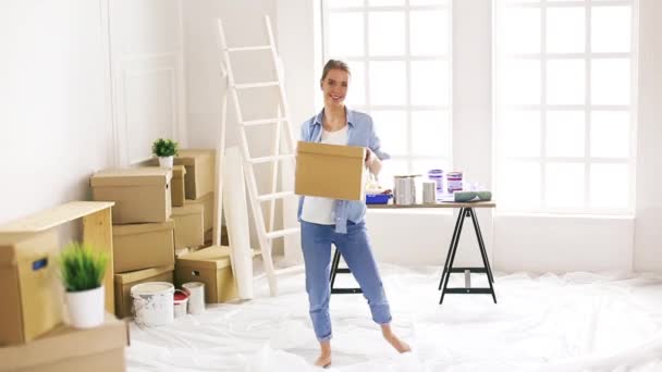 Een vrolijke jonge vrouw die in een nieuw huis intrekt, dansend met een doos. — Stockvideo