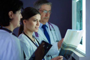 Bir grup doktor bir klinikte röntgenleri inceliyor, teşhis koymayı düşünüyorlar.