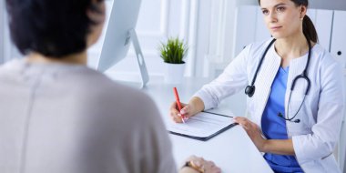 Doktor ve hasta hastane danışma odasında tıbbi sorunları tartışıyorlar. Doktor hasta formunu dolduruyor.
