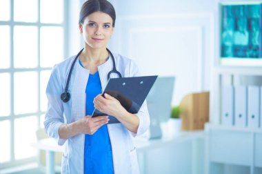 Doktor muayenehanesinde steteskopla gülümseyen genç bir bayan doktor.