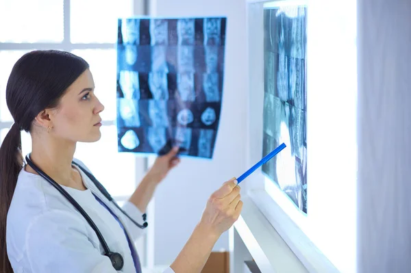 Junge lächelnde Ärztin mit Stethoskop zeigt auf Röntgenbild in Arztpraxis — Stockfoto