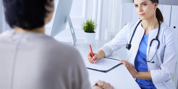 Dokter en patiënt bespreken medische problemen in een ziekenhuis spreekkamer. Doc vult een patiëntenformulier in — Stockfoto