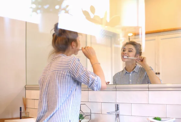 Jovem mulher bonita escovando os dentes na frente do espelho — Fotografia de Stock