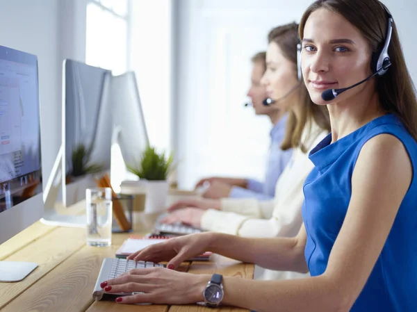 Portret van een jonge callcenter operator met een headset met collega 's die op kantoor op de achtergrond werken — Stockfoto