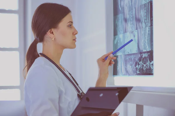 Mladý usměvavý ženský lékař se stetoskem ukazující na rentgen v ordinaci lékařů — Stock fotografie