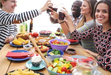 Ahşap masada otururken birlikte yemek yiyen bir grup insanın üst düzey görüntüsü. Masada yemek var. İnsanlar fast food yiyor..