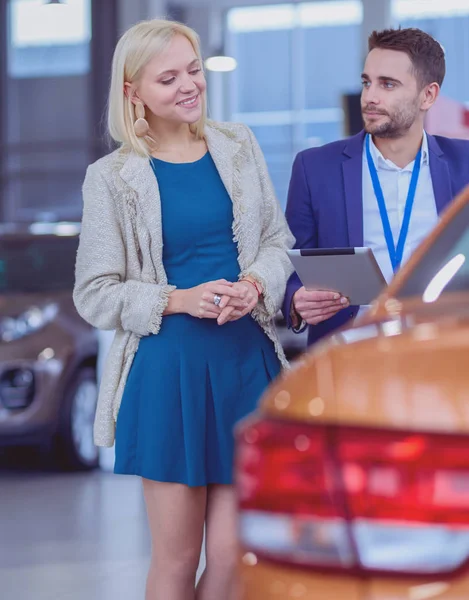 Negociante com mulher fica perto de um carro novo no showroom — Fotografia de Stock