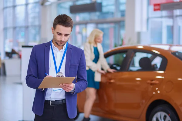 Vendedor fica perto de um carro novo no showroom — Fotografia de Stock