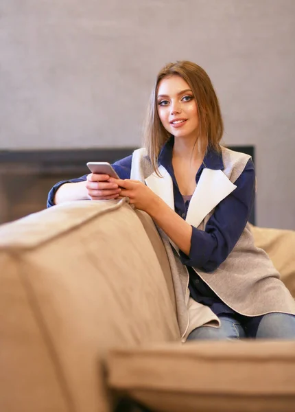 Jovem mulher sentada no sofá confortável com xícara de café em mãos na sala branca — Fotografia de Stock