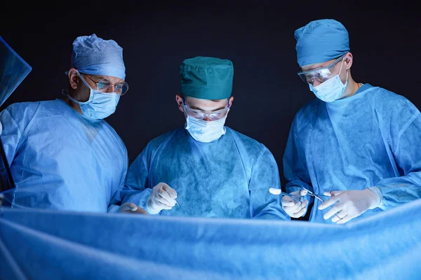 Grupo de cirurgiões no trabalho em sala de operações tonificada em azul. Equipe médica realizando operação — Fotografia de Stock