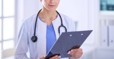 Doktor muayenehanesinde steteskopla gülümseyen genç bir bayan doktor.