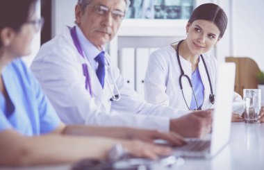 Parlak bir hastane odasında meslektaşlarıyla çalışan gülümseyen bir doktor.