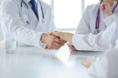 Doktor ofiste erkek bir hastayla el sıkışıyor.