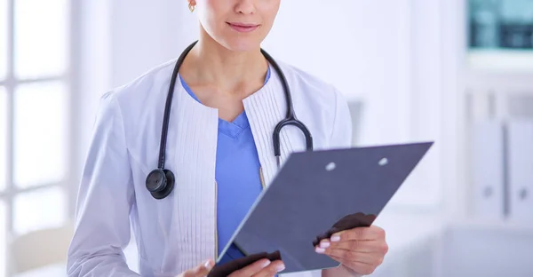 Joven doctora sonriente con estetoscopio sosteniendo una carpeta en el consultorio médico — Foto de Stock