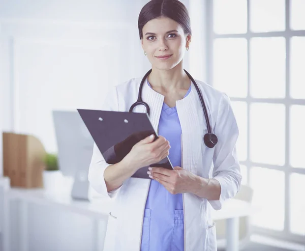 Mladá usměvavá doktorka se stetoskopem drží složku v ordinaci lékaře — Stock fotografie