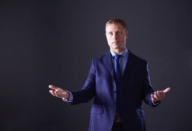 Başarılı, neşeli genç adamın portresi. Yeni ürünü sunuyor. Gri arka planda fotokopi spazmını gösteriyor.