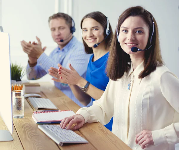 Portret van een jonge callcenter operator met een headset met collega 's die op kantoor op de achtergrond werken — Stockfoto