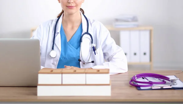 Bela jovem e sorridente médica sentada na mesa e escrevendo. médico feminino — Fotografia de Stock