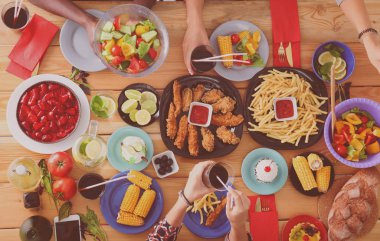 Ahşap masada otururken birlikte yemek yiyen bir grup insanın üst düzey görüntüsü. Masada yemek var. İnsanlar fast food yiyor..