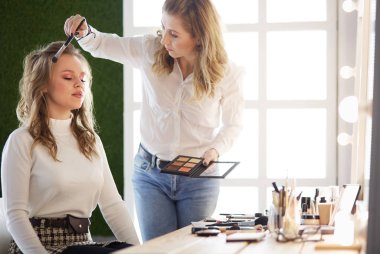 Makyaj sanatçısı genç ve güzel gelinin makyajını yapıyor.