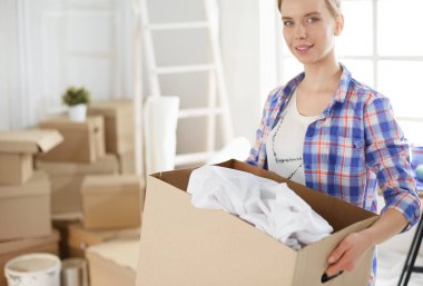 Young woman moving house to new home holding cardboard boxes clipart