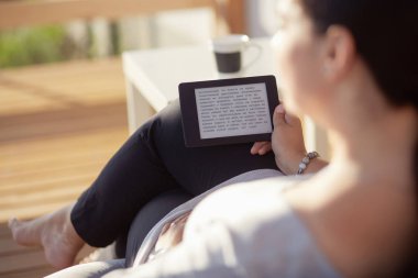 Touchpad ile kanepede oturan gülümseyen genç kadın.