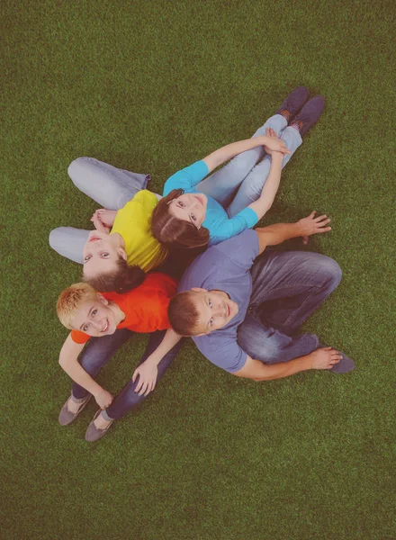Grupa młodych ludzi siedzi na zielonej trawie — Zdjęcie stockowe