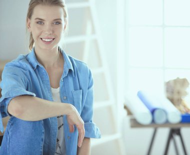 Genç bir kadın boş bir odada beyaz bir sandalyede oturuyor, bir şeyler düşünüyor.