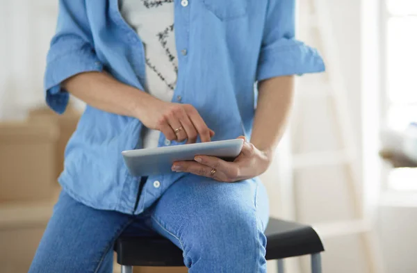 Młoda kobieta siedzi w domu i kupuje nowe meble przez Internet za pomocą tabletu — Zdjęcie stockowe