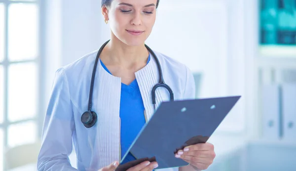 Joven doctora sonriente con estetoscopio sosteniendo una carpeta en el consultorio médico — Foto de Stock