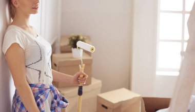 Mutlu gülümseyen kadın yeni evin iç duvarını boyuyor.