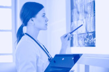 Stetoskop lu genç gülümseyen kadın doktor doktor ofisinde röntgeni işaret ediyor