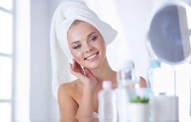 Bornozlu genç kadın banyo aynasına bakıyor.