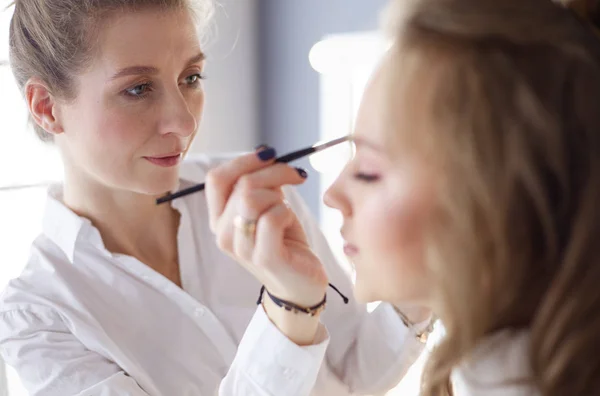 Giovane bella sposa che applica il trucco nuziale da truccatore professionista — Foto Stock