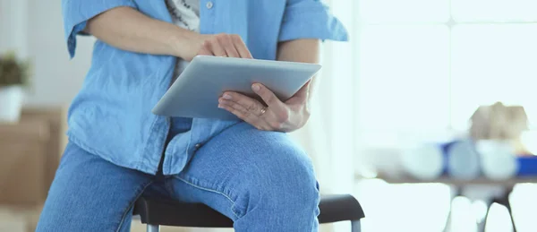 Genç bir kadın evde oturuyor ve tablet bilgisayar kullanarak internetten yeni mobilyalar alıyor. — Stok fotoğraf