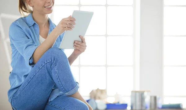 若い女性が家に座ってタブレットコンピュータを使用してインターネット上で新しい家具を購入します。 — ストック写真