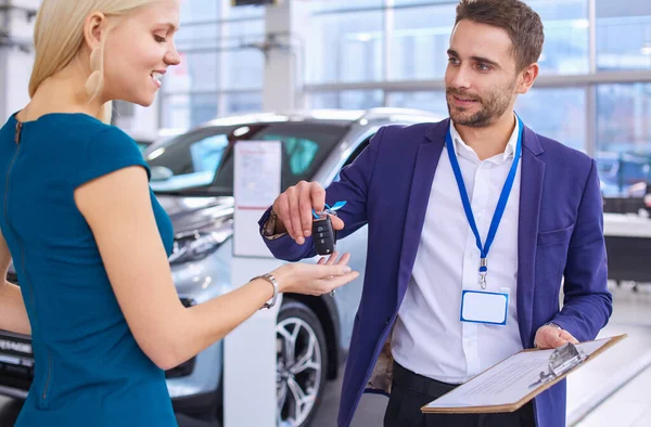 Car salesman sells a car to happy customer in car dealership and hands over the keys