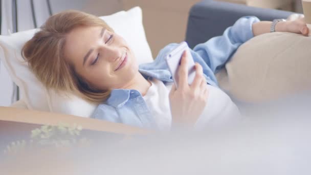 Menina bonita relaxante no sofá de couro e usando telefone celular — Vídeo de Stock