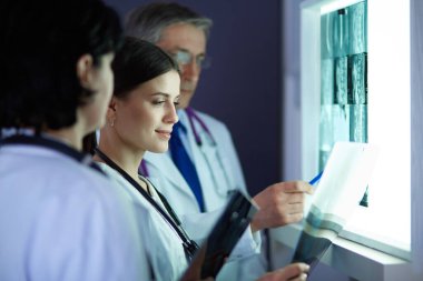 Bir grup doktor bir klinikte röntgenleri inceliyor, teşhis koymayı düşünüyorlar.