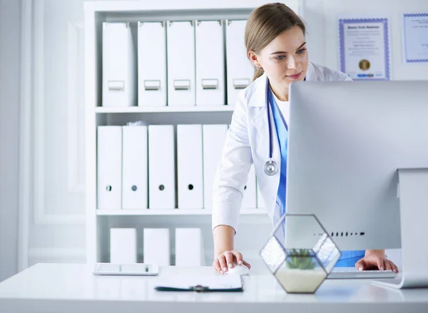 Portrait of female physician using laptop computer while standing near reception desk at clinic or emergency hospital