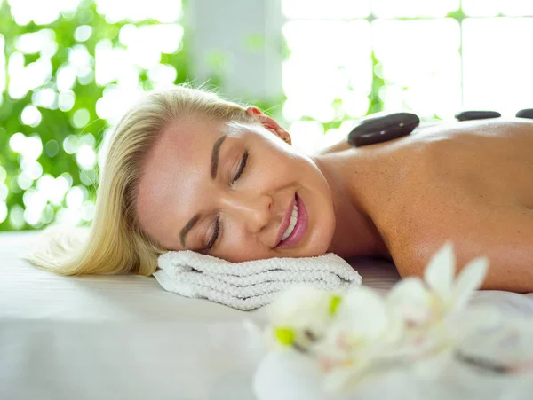 Mulher bonita com os olhos fechados recebendo massagem de pedra quente no spa do salão — Fotografia de Stock