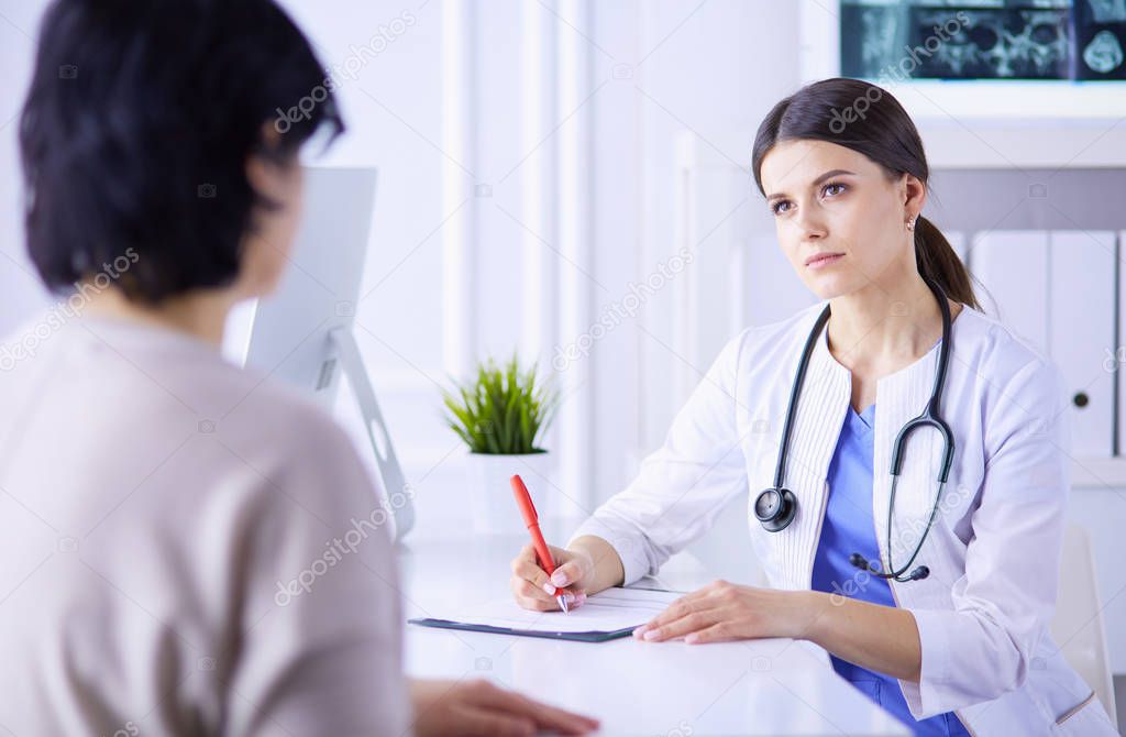 Doctor and patient discussing medical problems in a hospital consulting room. Doc filling in a patients form